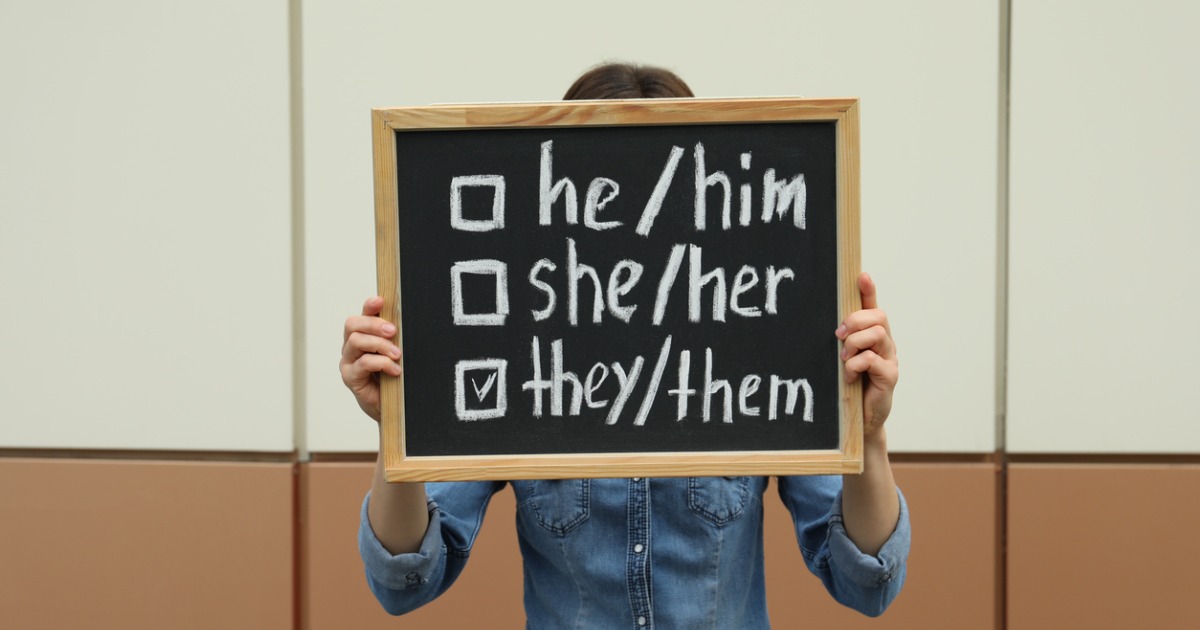 A person holds a chalkboard that has he/him, she/her and they/them written on it