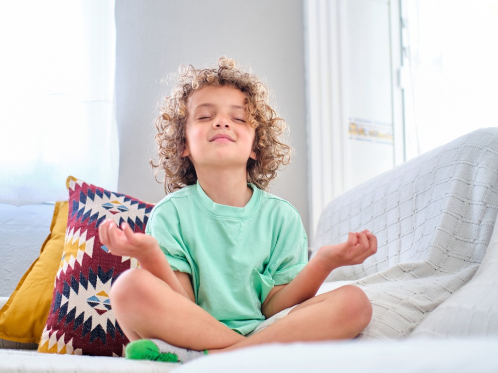 Young boy, practicing meditation on sofa, eyes shut, smiling