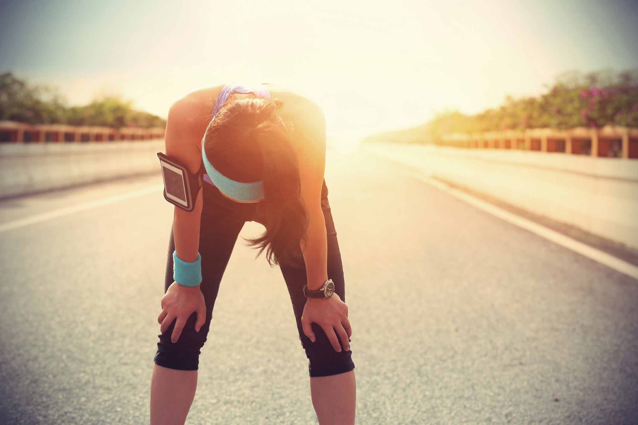 Young adult female runner bent over, overheated, outside