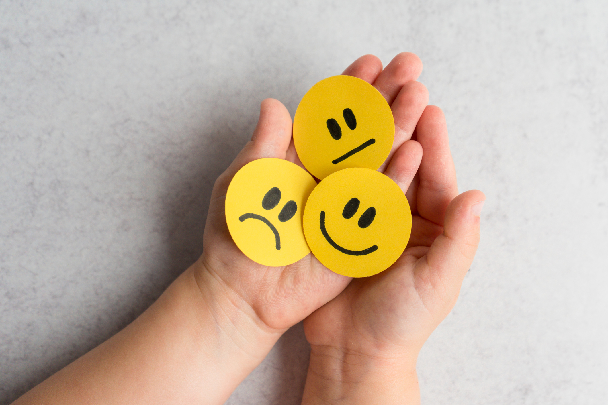 A child holding smiley faces showing different expressions. 