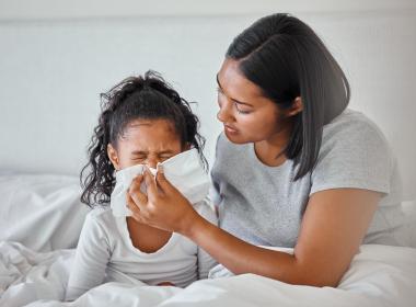 Mom helping sick daughter blow nose in bed