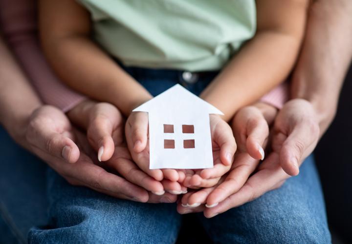 Hands holding a paper cutout of a house.