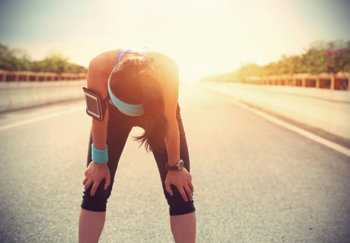 Young adult female runner bent over, overheated, outside