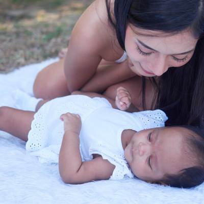 Mom and infant baby outside on blanket, wearing white.