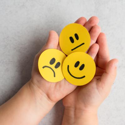 A child holding smiley faces showing different expressions. 